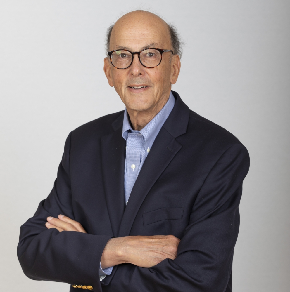 Portrait of Roger Glass '63 wearing a navy blazer over a light-blue shirt with his arms folded.