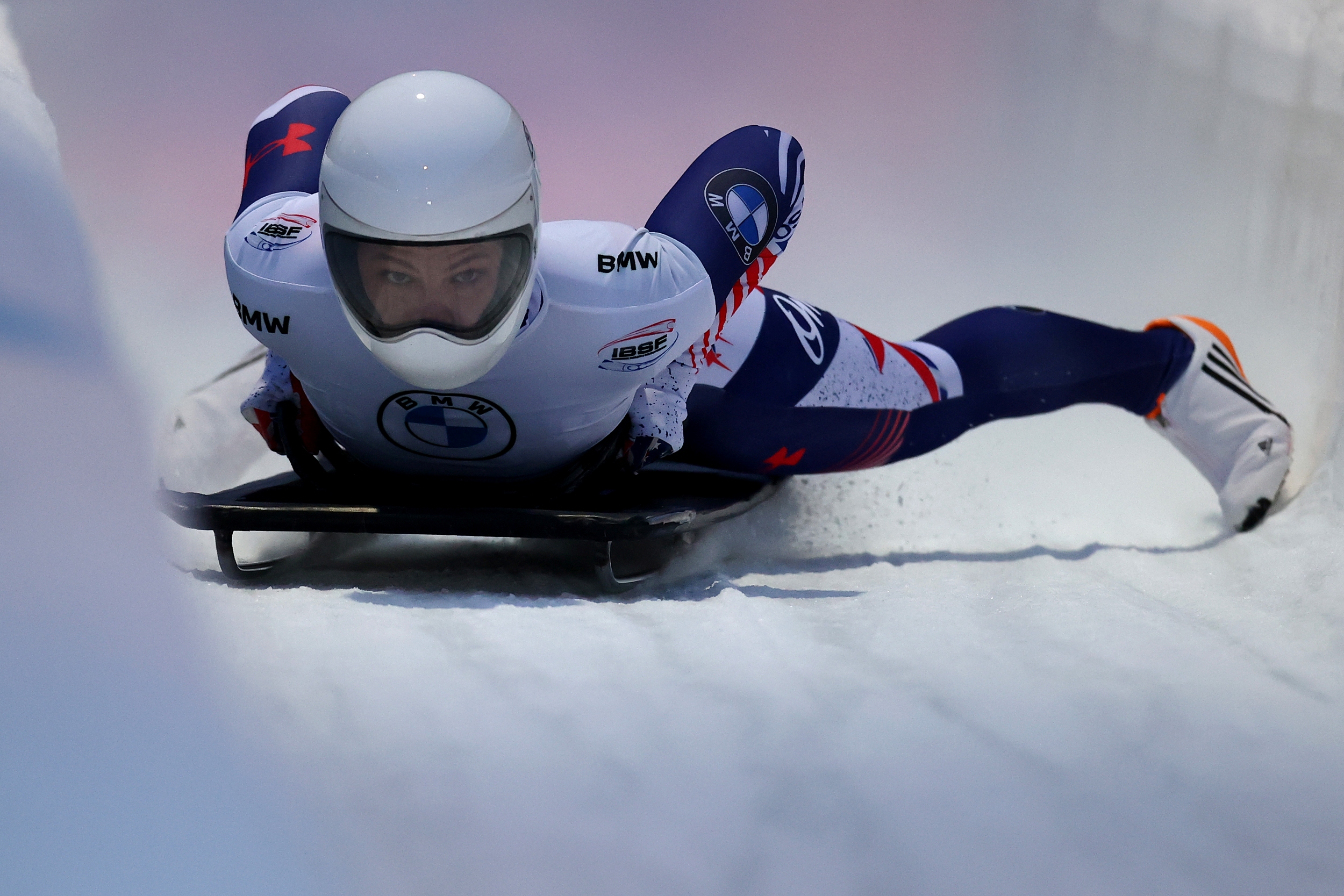 Kelly Curtis '08, in a white helmet and white, red, and blue form-fitting spandex sliding uniform, moves downhill on her skeleton apparatus.